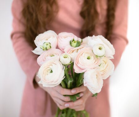 A girl in a pink dress is holding a bouquet of delicate Ranunculus flowers. Romantic photo.