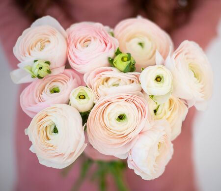 A girl in a pink dress is holding a bouquet of delicate Ranunculus flowers. Romantic photo.の写真素材