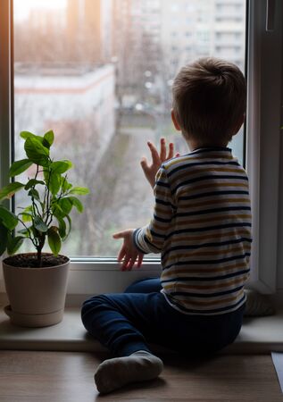 The boy is sitting on the window sill. Sad mood. Sit at homeの写真素材