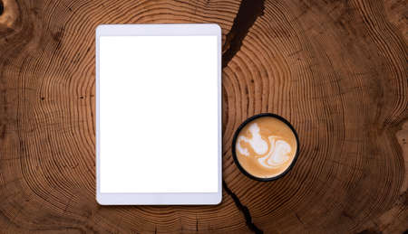 A white tablet with an empty screen and a Cup of coffee on a wooden table.の写真素材