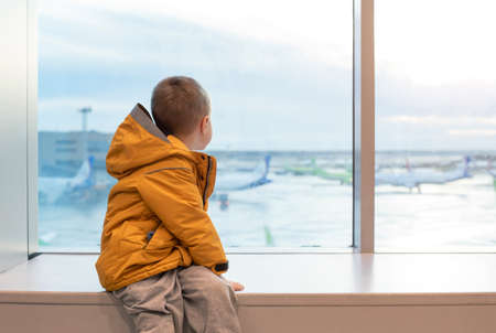 A boy in a yellow jacket at the airport at the big window.の写真素材