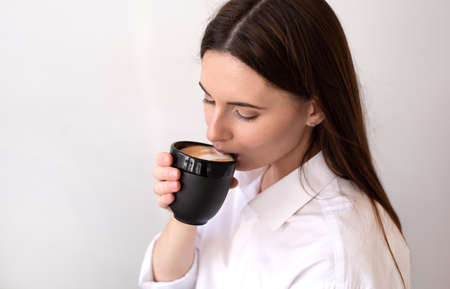 Young beautiful woman with a Cup of coffee in her hands. Bright interior of the cafe.