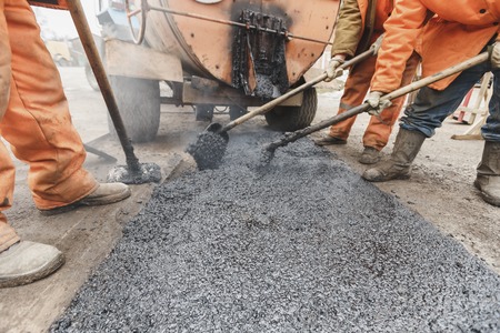 Working men in orange overalls repairing the road, shovels fill asphalt road repairの写真素材