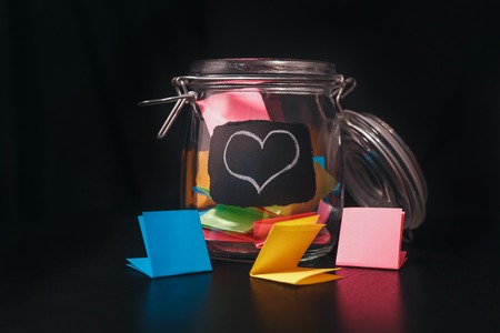 Open Bank with colorful stickers on a black background with white chalk-drawn heartの写真素材