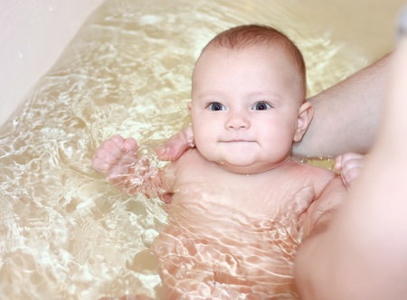 Beautiful happy baby girl bathing. Father holding six month babyの写真素材