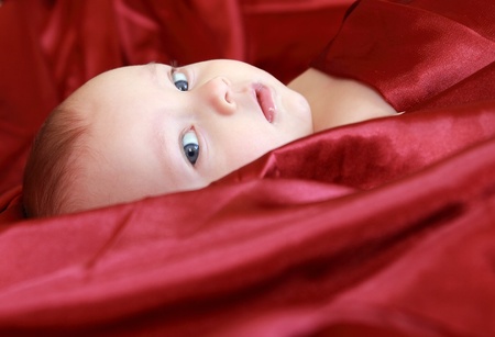 Adorable baby looking out of the red bright covered with big interest の写真素材