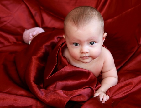 Beautiful baby girl lying on the bright dark red blanketの写真素材