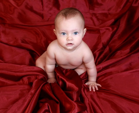 Portrait of blue eyes beautiful baby girl looking in camera and sitting on dark red sheetsの写真素材