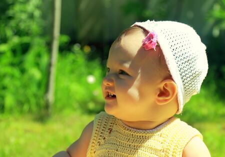Closeup portrait of fun smiling baby girl in hat on green grass backgroundの写真素材