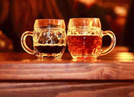 Two beer glasses on wooden table in bar  Dark and lager tasty beer
