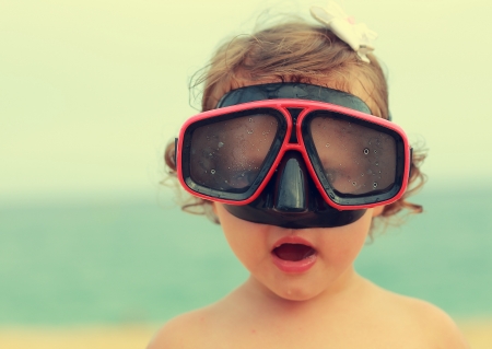 Surprising baby girl in diving mask looking fun on blue sea backgroundの写真素材