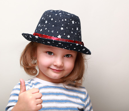 Cute kid girl in blue hat showing thumb up signの写真素材