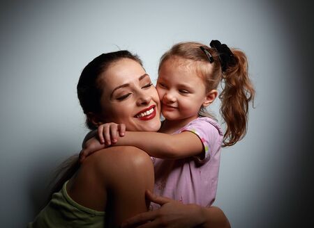 Beautiful smiling young mother cuddling her cute daughter on dark background. Contrast portraitの写真素材