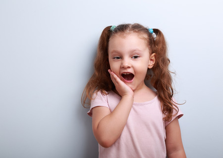 Surprising fun girl looking with open mouth on blue background