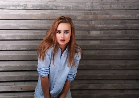 Beautiful woman with red long hair style posing in blue shirt and jeans on street wall backgroundの写真素材