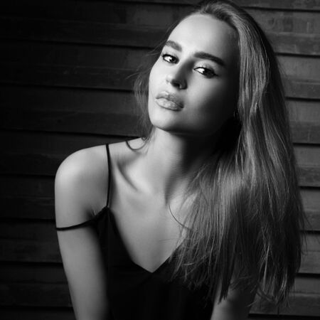 Beautiful charming woman lookin sexy with long hair on dark background. Black and white portraitの写真素材