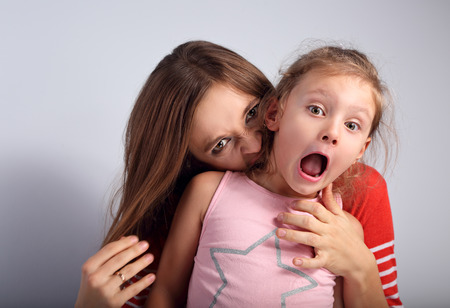 Angry emotional young mother wanting to bite her naughty capricious daughter with screaming nervous frightened face and open mouth on blue background. Humor concept portraitの写真素材