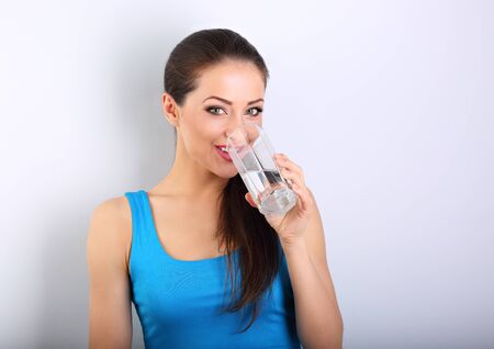 Young beautiful woman drinking fresh pure water from glass on blue backgroundの写真素材