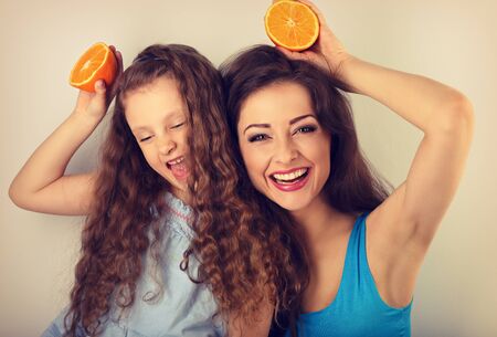 Grimacing joying humor young mother and cute long hair daughter holding slices of fresh bright oranges in hands and playing the ape. Healthy and diet lifestyle. closeup vintage toned portraitの写真素材