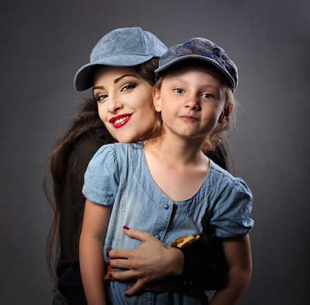 Happy smiling mother and daughter posing in blue baseball caps on dark shadow grey backgroundの写真素材