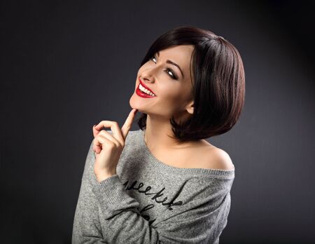 Thinking makeup business woman looking up with toothy natural smiling on dark grey background. Short hair style. Closeupの写真素材