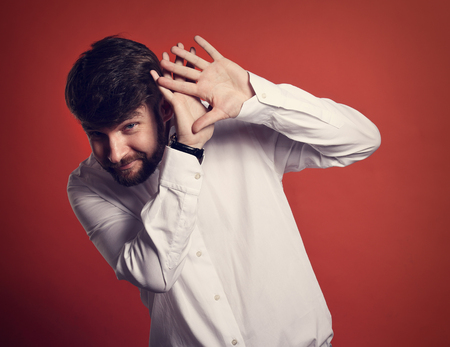 Stressed unhappy frightened bearded business man defends himself the hands in white shirt on red...