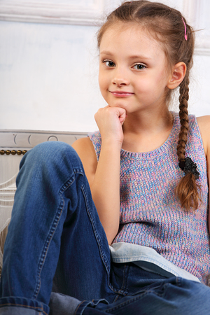 Beautiful thinking cute kid girl sitting on the bench in blue jeans and looking happy. Closeup portraitの写真素材