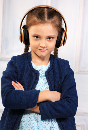 Happy calm serious kid girl in blue jacket listening the music in wireless headphone on studio background. Closeupの写真素材