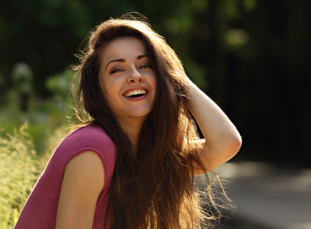 Beautiful toothy laughing enjoying young woman looking with long bright hair on nature bright sunny summer background. Closeup portraitの写真素材