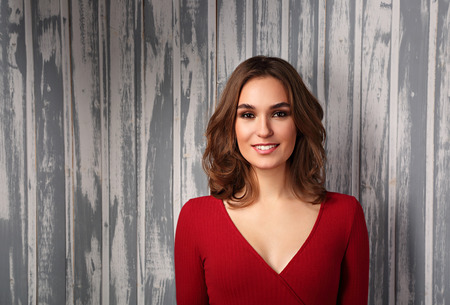 Beautiful positive toothy smiling woman and looking happy in casual red shirt and short curly hair on empty copy space background.の写真素材
