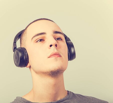 Young teen guy listening the misic on black wireless headphones with fun happy face. Closeup portraitの写真素材