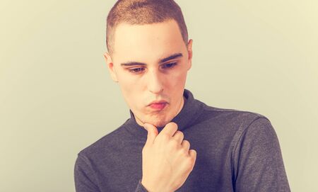 Sad unhappy young man thinking with hand under the face and looking down. Vintage closeup toned color portraitの写真素材