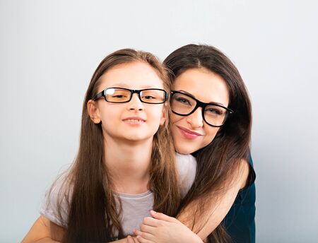 Happy young casual mother and smiling kid in fashion glasses hugging on light blue background with empty copy space. Closeup studio portraitの写真素材
