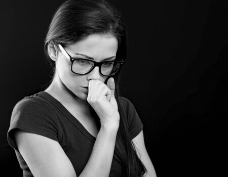 Unhappy worried woman in glasses holding the hand under the face and find the solution on problem situation. Coronavirus. Studio portrait on black backgroundの写真素材