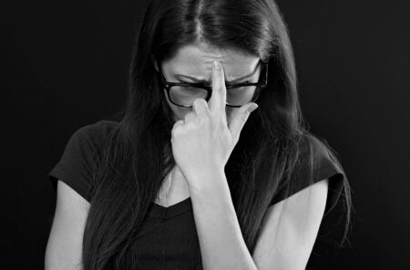 Unhappy worried woman in glasses holding the hand under the face and find the solution on problem situation. Coronavirus. Studio portrait on black backgroundの写真素材