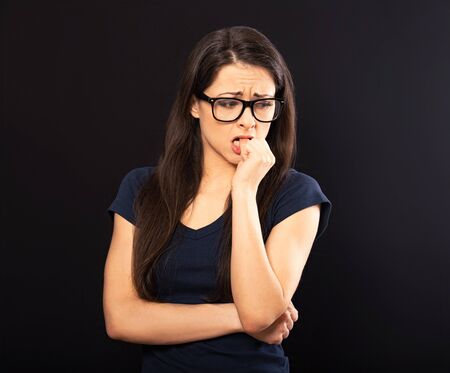 Unhappy worried woman in glasses holding the hand under the face and find the solution on problem situation. Coronavirus. Studio portrait on black backgroundの写真素材