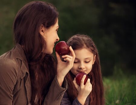 Happy smiling woman and fun kid have a picnic and holding the green apples in hands on summer green grass evening background. Closeup portraitの写真素材