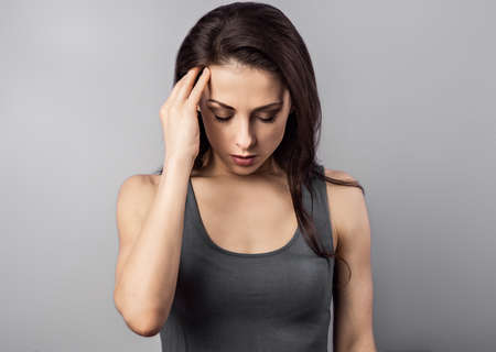 Depressed woman holding the hand the head. Cold, flu, virus, tonsillitis, respiratory disease, quarantine, epidemic concept portrait. Beautiful caucasian young woman. Closeup portraitの写真素材