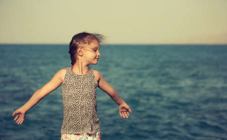 Small kid girl relaxing and gesturing the arms sign like a bird wanting to fly on blue sea background. Closeup holidays portraitの写真素材