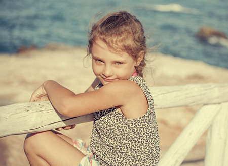 Tired from sunny weather kid girl looking unhappy and wanting to rest on blue sea background and vacation sky. Closeup holidays outdoors portraitの写真素材