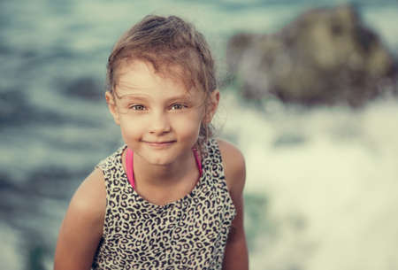 Happy kid girl smiling and joying on blue sea background and vacation sky. Closeup holidays outdoors portraitの写真素材