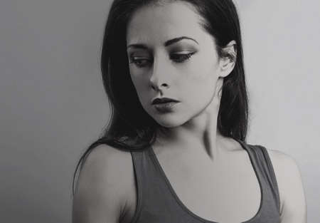 Unhappy depressed woman looking down. Tired female model. Art color. Black and white. On gray background with empty copy space. Closeup. Conceptual portrait. Shadow and lightの写真素材