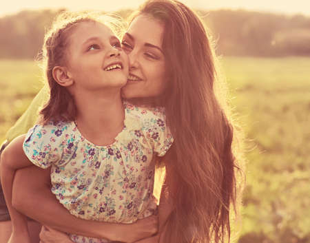 Happy enjoying mother hugging her playful laughing kid girl in sunset sunny light on summer background in bright yellow colors. Closeup portraitの写真素材
