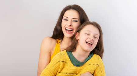 Happy mother and smiling kid girl laughing together on blue light background. Closeup portraitの写真素材
