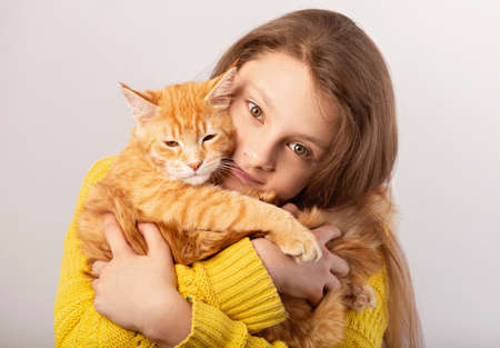 Happy kid girl holding on the hands her red maine coon kitten and hugging with love. Closeup portrait on toned vintage backgroundの写真素材