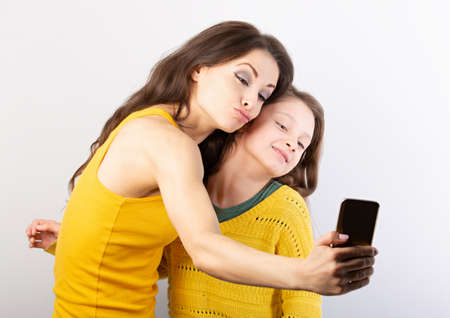 Happy mother and smiling kid girl laughing together and making self photo on mobile phone on blue...