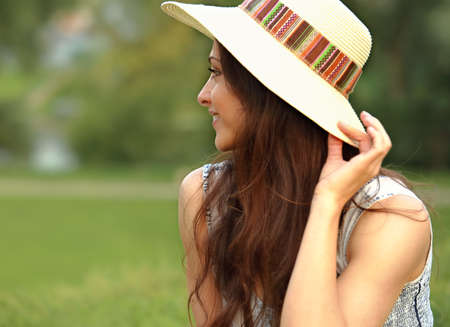 Beautiful smiling woman in hat looking outdoors summer green trees background. Closeup portrait. Profile viewの写真素材