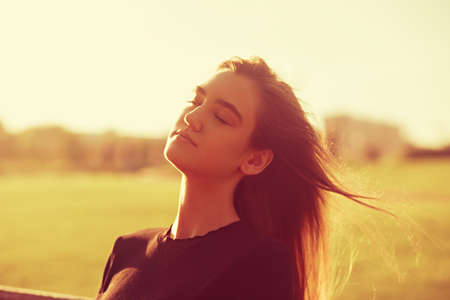 Beautiful relaxing woman with closed eyes is deep breathing and with long amazing hair on nature bright sunset summer background. Closeup toned portraitの写真素材