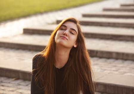Beautiful relaxing woman with closed eyes is deep breathing and with long amazing hair on nature bright sunset summer background. Closeup toned portraitの写真素材
