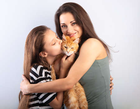 Happy young mother hugging her red maine coon kitten and daughter. Closeup portrait of smiling familyの写真素材
